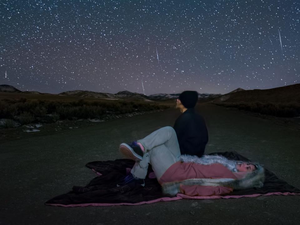 Yound adults look up at the sky, wearing heavy winter clothes and laying on a blanket.