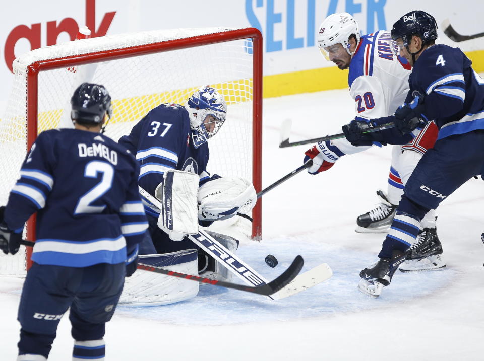 Winnipeg Jets goaltender Connor Hellebuyck (37) makes a save against New York Rangers' Chris Kreider (20) as Jets' Neal Pionk (4) defends during the second period of an NHL hockey game Friday, Oct. 14, 2022, in Winnipeg, Manitoba. (John Woods/The Canadian Press via AP)