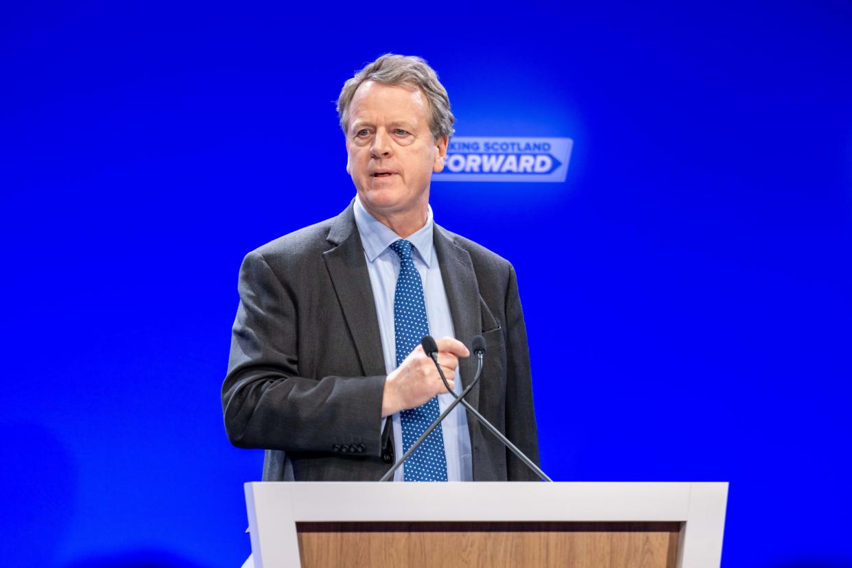 Alister Jack speaking from a lectern with Conservative signage behind him