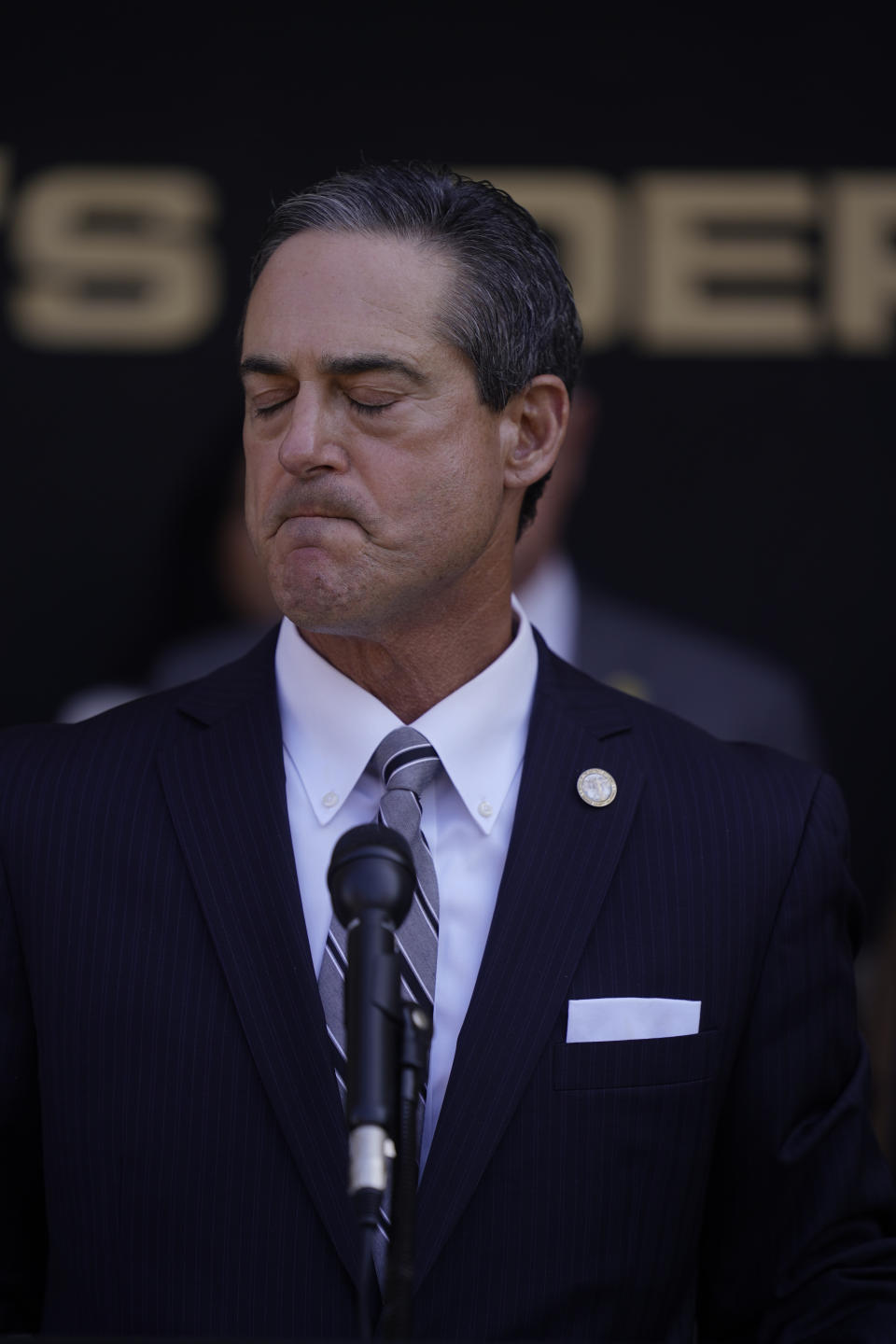 Orange County District Attorney Todd Spitzer, at podium, grimaces as he speaks about the shooting at Cook's Corner, a place he rides his motorcycle in rural Trabuco Canyon, Calif., in Orange County, during a news conference in Santa Ana, Calif., Thursday, Aug. 24, 2023. (AP Photo/Damian Dovarganes)