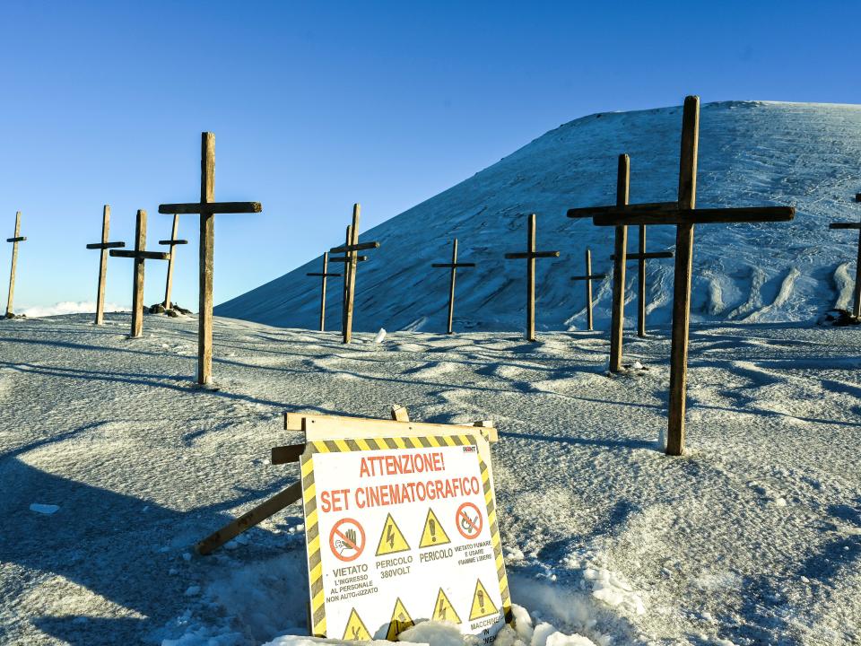 wooden crosses in the snow on mount etna on the cyrano set, there's a sign in italian in the foreground that reads "attention! set cinematografico"