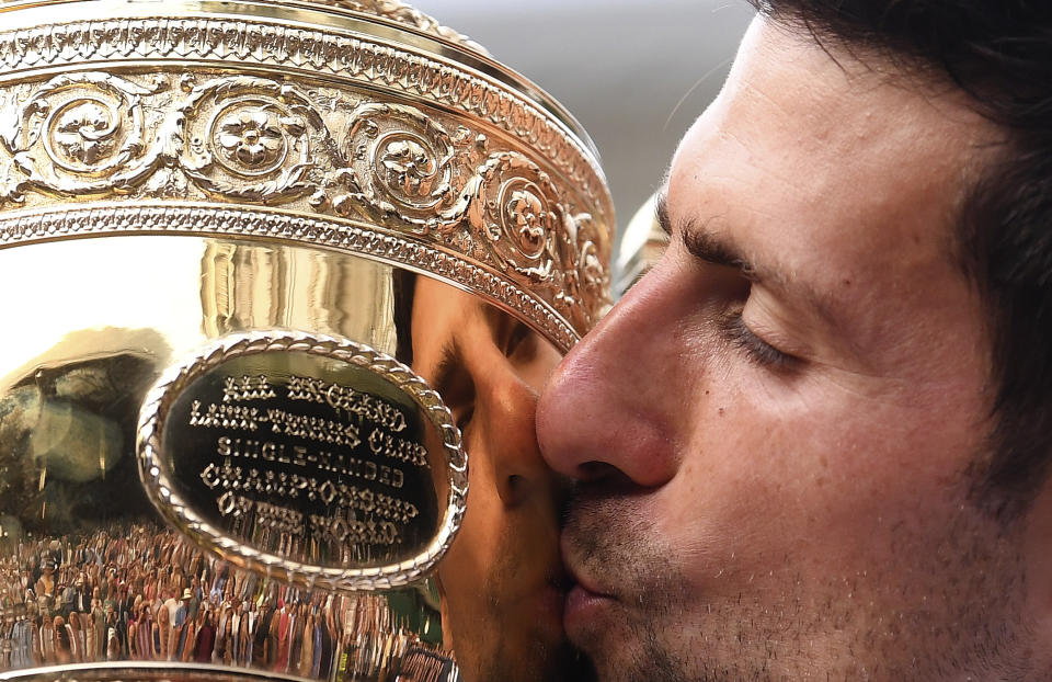 FILE - In this July 14, 2019, file photo, Serbia's Novak Djokovic kisses the trophy during the presentation after he defeated Switzerland's Roger Federer in the men's singles final match of the Wimbledon Tennis Championships in London. The All England Club says it plans to make a decision next week whether to postpone or cancel Wimbledon because of the coronavirus pandemic. (Laurence Griffiths/Pool Photo via AP, File)