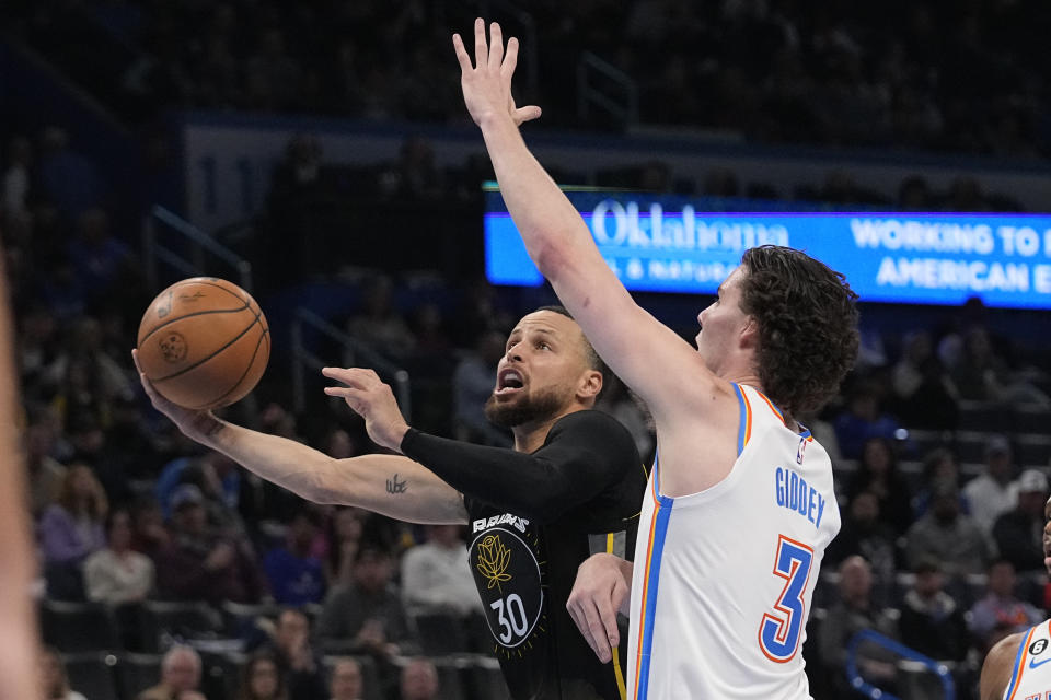 Golden State Warriors guard Stephen Curry, left, goes to the basket past Oklahoma City Thunder guard Josh Giddey (3) in the first half of an NBA basketball game Tuesday, March 7, 2023, in Oklahoma City. (AP Photo/Sue Ogrocki)