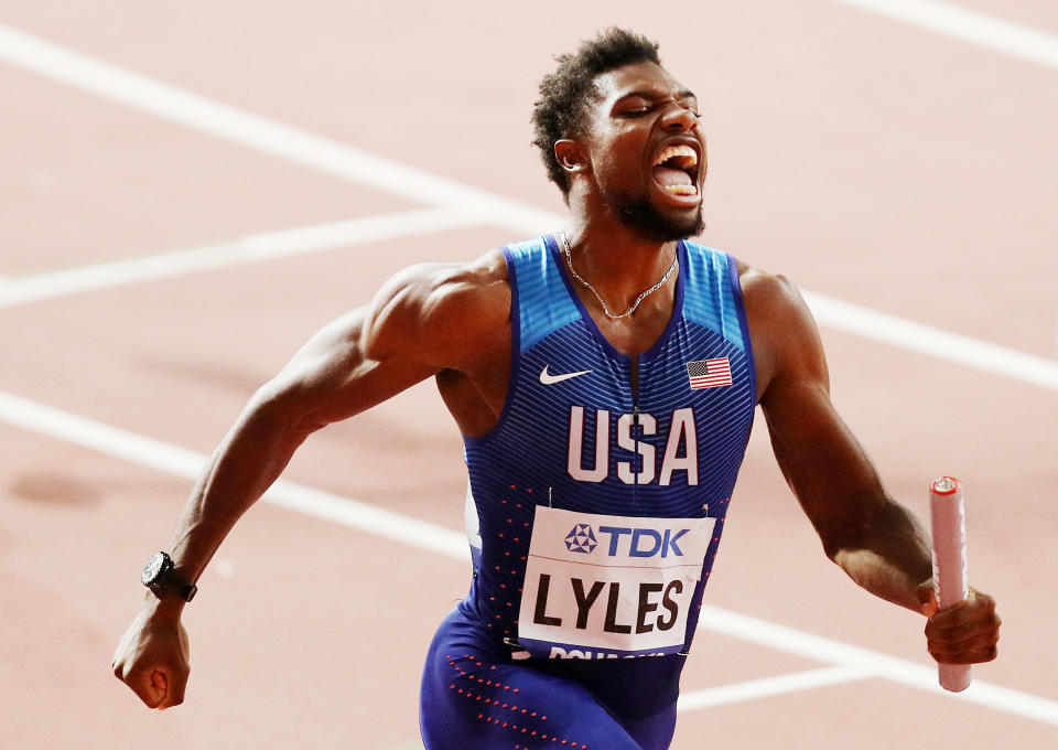 Noah Lyles cheers while he runs with a baton