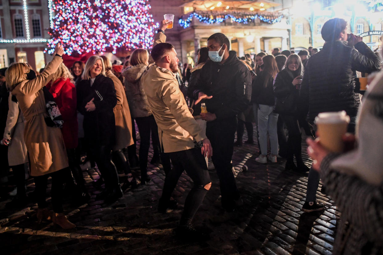 LONDON, ENGLAND  - DECEMBER 05: A man not wearing a mask dances in front of a man wearing a mask in Covent Garden on December 5, 2020 in London, England. On Tuesday night, Dec 1, MPs voted in favour of government proposals to enter England into a tiered system of lockdown beginning at midnight. Residents of Tier Two - High Alert can socialise with anyone they live with or who is in their support bubble in any indoor setting, whether at home or in a public place. Outdoors they must observe the rule of six. Pubs and bars must close, unless operating as restaurants. Hospitality venues can only serve alcohol with substantial meals and must close between 11pm and 5am with last orders called at 10pm. Organised indoor sport, physical activity and exercise classes will be permitted if it is possible for people to avoid mixing with people they do not live with. Schools remain open. (Photo by Peter Summers/Getty Images)