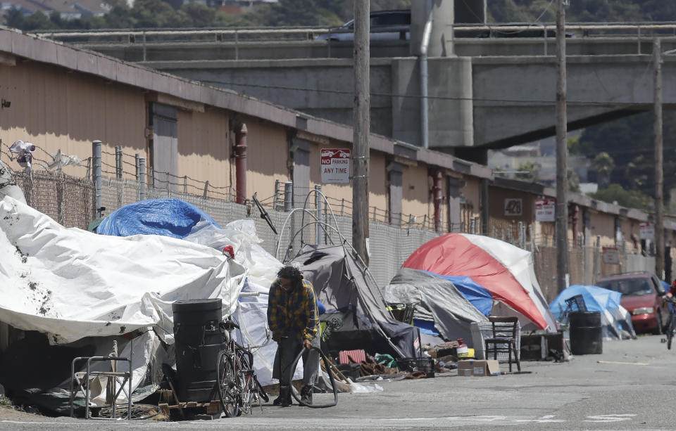 This Thursday, June 27, 2019, photo shows a man holding a bicycle tire outside of a tent along a street in San Francisco. A federally mandated count of homeless in San Francisco increased 17% in two years, driven in part by a surge of people living in RVs and other vehicles. (AP Photo/Jeff Chiu)