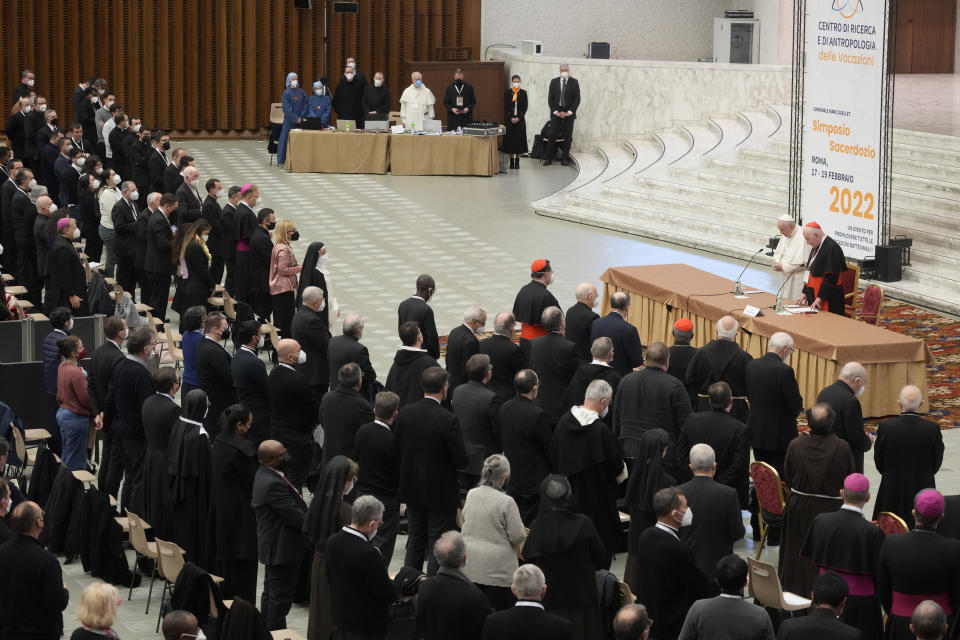 Pope Francis, standing at left at the table, and Cardinal Marc Ouellet attend the opening of a 3-day Symposium on Vocations in the Paul VI hall at the Vatican, Thursday, Feb. 17, 2022. (AP Photo/Gregorio Borgia)