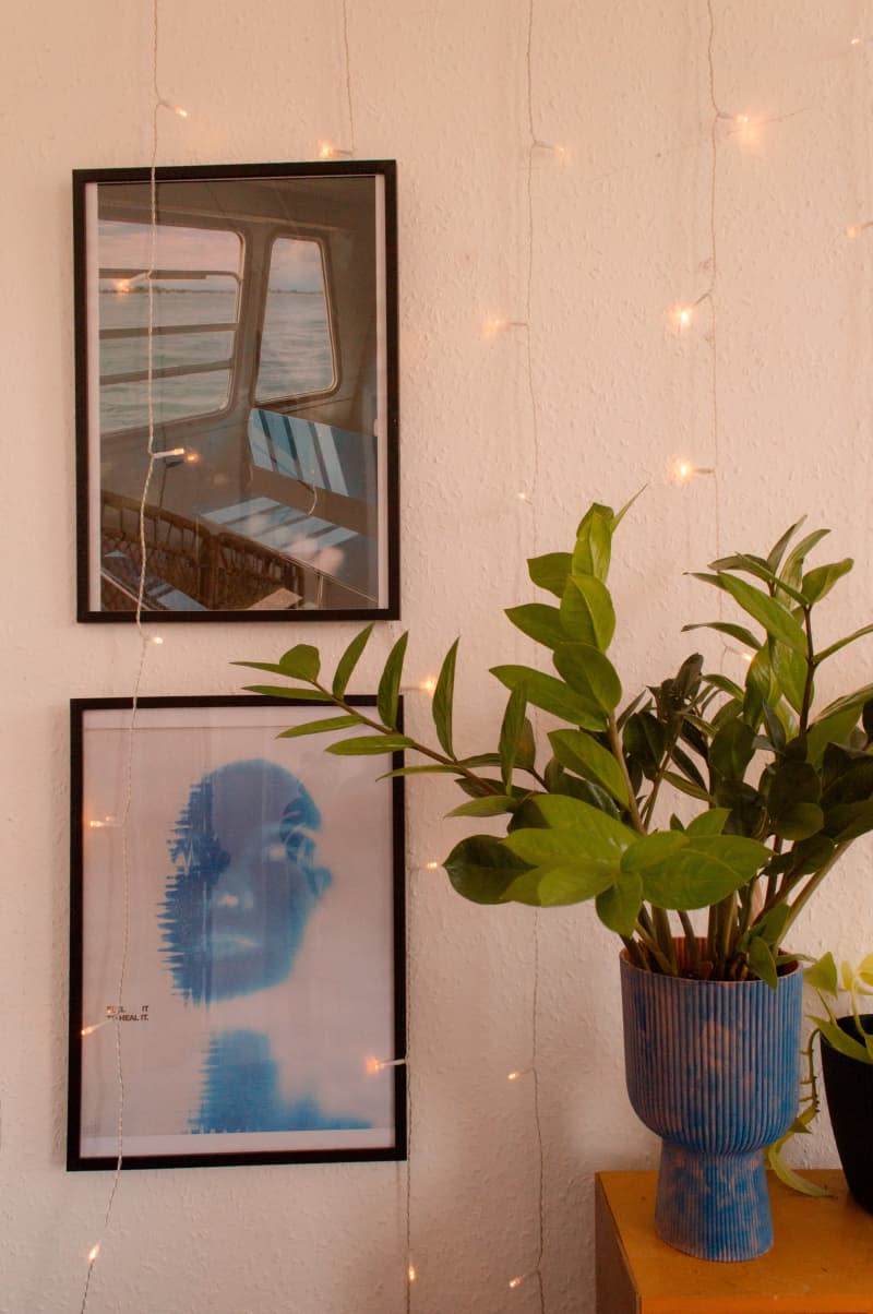 Two framed images images next to plants in a a blue vase.