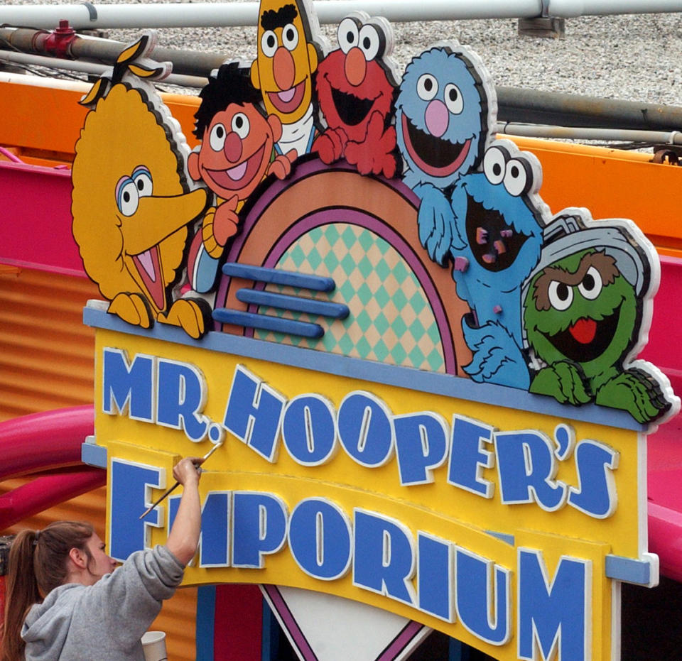 FILE - In this May 4, 2005, file photo, Tessa Meier puts some new paint on the sign outside Mr. Hooper's Emporium to get ready for opening day at Sesame Place in Langhorne, Pa. Officials with SeaWorld Entertainment and Sesame Workshop announced Monday, Oct. 21, 2019, that they are opening the country’s second Sesame Place park in San Diego in 2021. The first Sesame Place opened almost 40 years ago outside Philadelphia. (Harry Sircely/Bucks County Courier Times via AP, File)