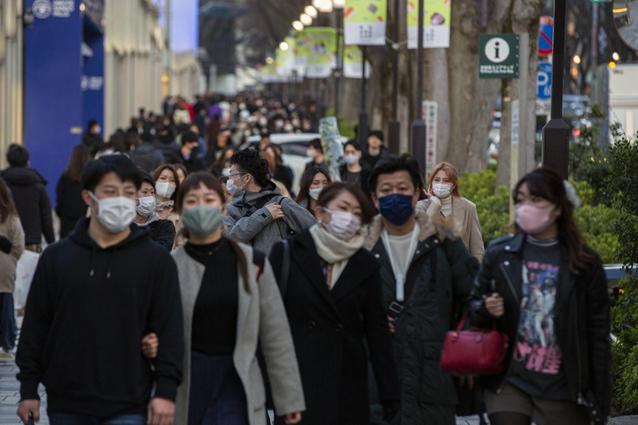 Personas con tapabocas para ayudar a frenar la propagación del coronavirus caminan por una vereda en un distrito comercial de Tokio, el domingo 28 de febrero de 2021