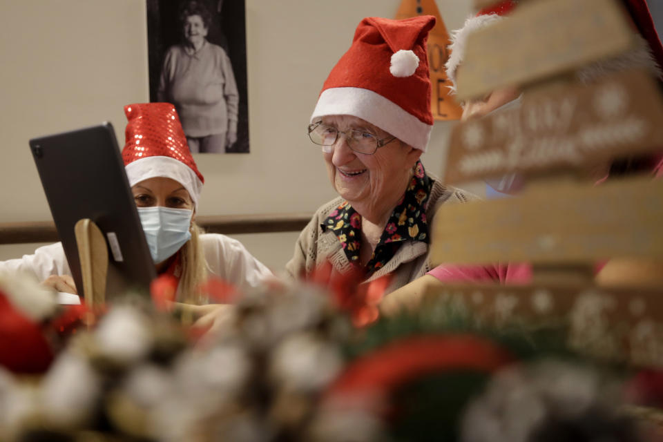 Giuseppina Foresti, 93, is flanked by director Maria Giulia Madaschi, as she talks on a video call with Elisabetta Cervi, a donor unrelated to her, who bought and sent her a bracelet as Christmas present through an organization dubbed "Santa's Grandchildren", at the Martino Zanchi nursing home in Alzano Lombardo, one of the area that most suffered the first wave of COVID-19, in northern Italy, Saturday, Dec. 19, 2020. (AP Photo/Luca Bruno)