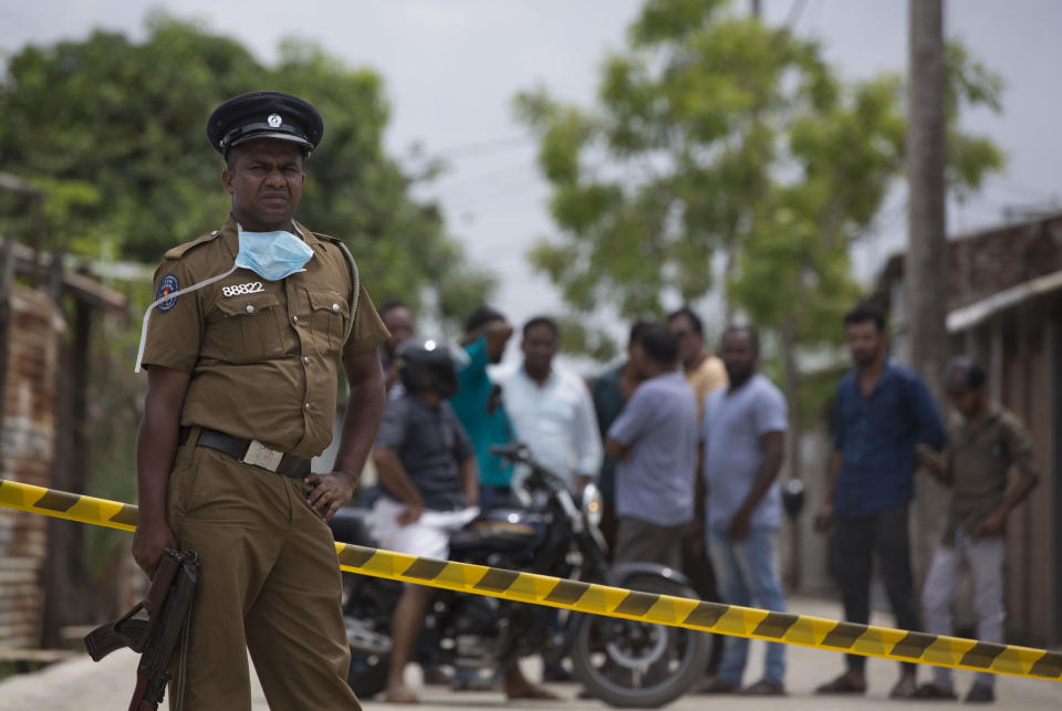 A police officer stand guards at a site of a gun battle between troops and suspected Islamist militants as neighbors gather to watch in Kalmunai, Sri Lanka, Sunday, April 28, 2019. Police in Ampara showed The Associated Press on Sunday the explosives, chemicals and Islamic State flag they recovered from the site of one security force raid in the region as Sri Lanka's Catholics celebrated at televised Mass in the safety of their homes. (AP Photo/Gemunu Amarasinghe)