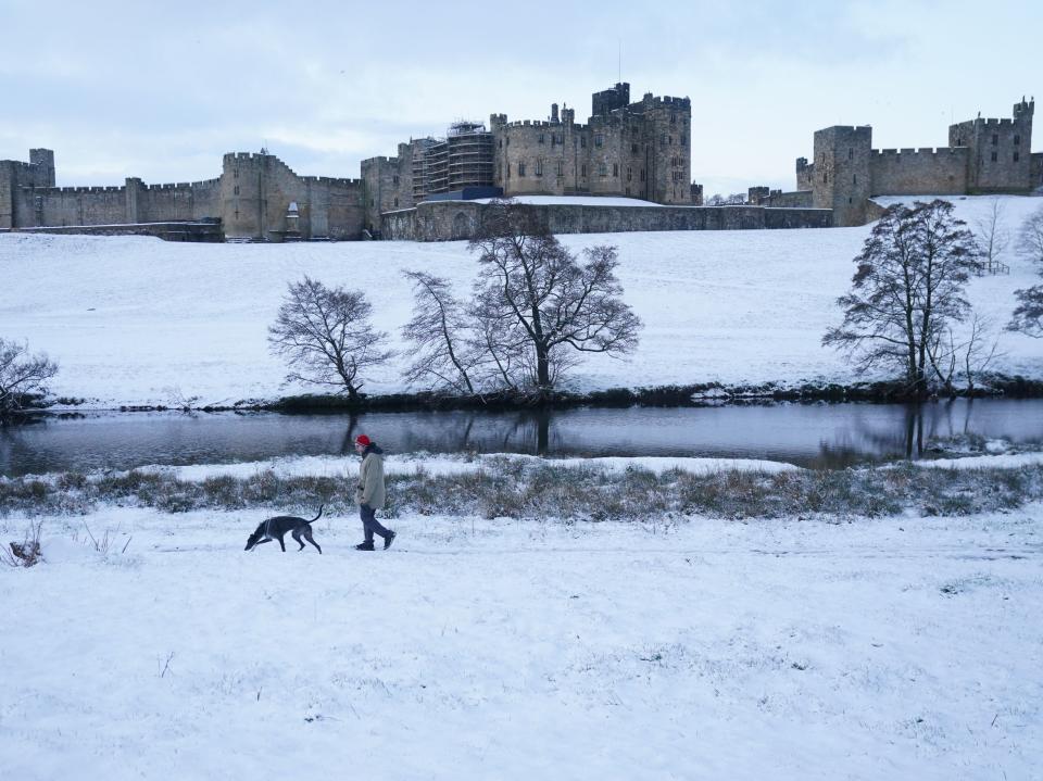 A man walks his dog through a snow covered field at Alnwick Castle in Northumberland (PA)