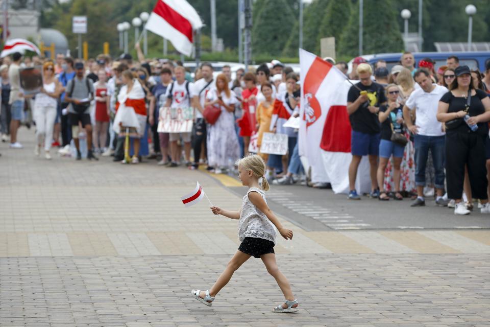 A girl walks holding a small old Belarusian national flag as activists greet and support workers leaving the Minsk Tractor Works Plant after their work shift in Minsk, Belarus, Tuesday, Aug. 18, 2020. Workers in Belarus are joining a growing strike, turning up pressure on the country's authoritarian leader to step down after winning an election they say was rigged. (AP Photo/Sergei Grits)