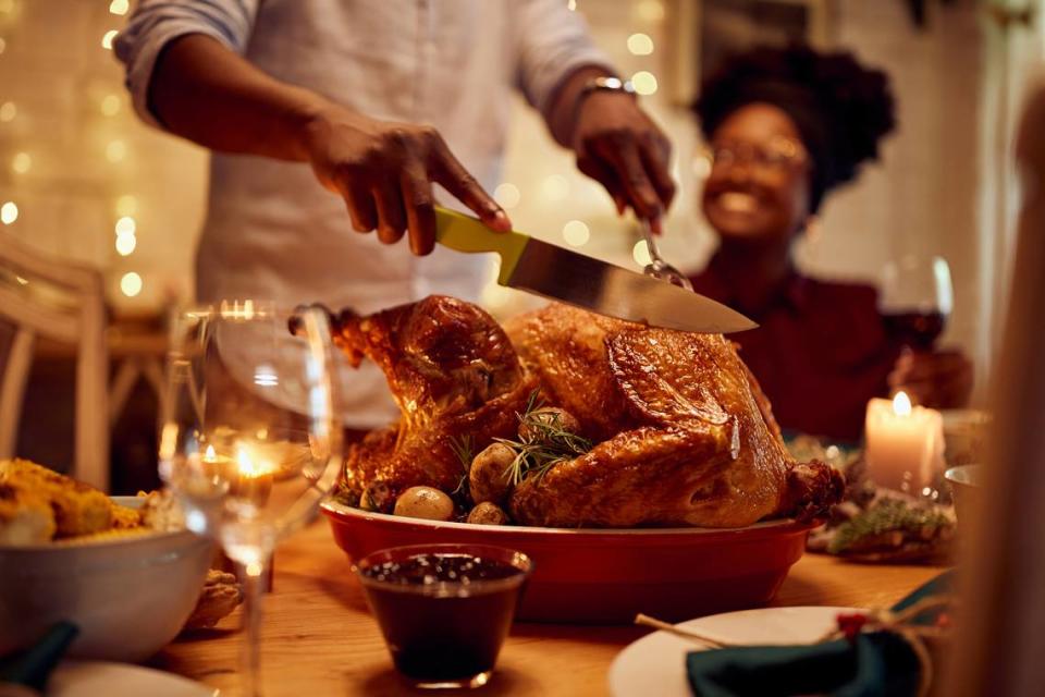 Close-up of black man carving roasted turkey during Thanksgiving meal at dining table.