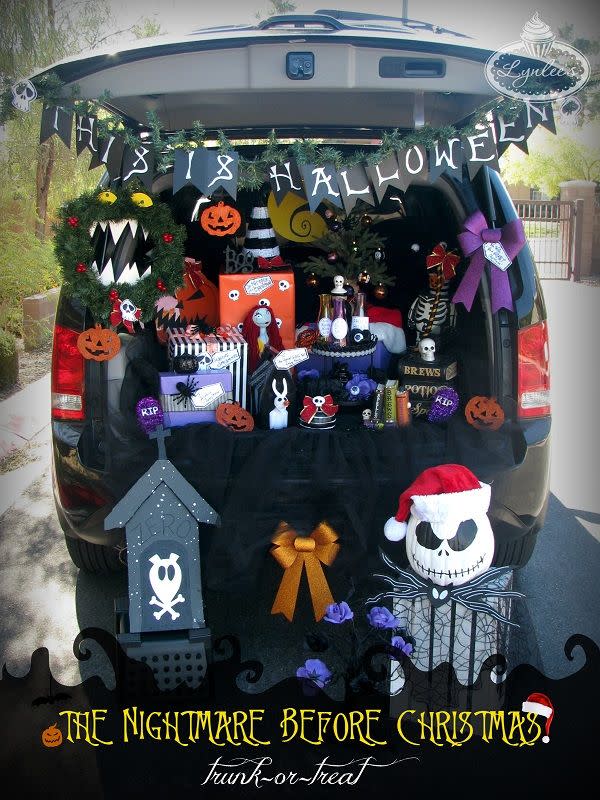open tailgate with this is halloween banner hanging from it, christmas wreath with teeth, purple bow, and in the back of the vehicle are pumpkin cut outs, wrapped presents in purple, black and white stripes and orange paper, potion bottle with handmade labels, and more, in front of the vehicle is a dog house made from a foam tombstone and jack skellington's face on a white pumpkin with a santa hat