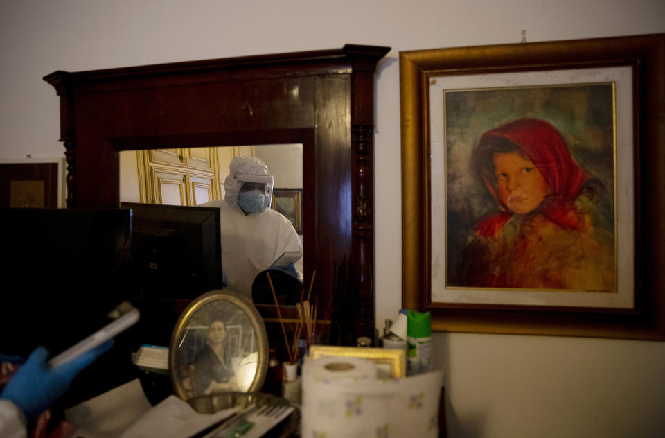 Nurse Gabriele Cremona, Doctor Luigi Cavanna's assistant, is reflected in a mirror as he waits in the home of a COVID-19 patient, in Monticelli d'Ongina, near Piacenza, Italy, Wednesday, Dec. 2, 2020. (AP Photo/Antonio Calanni)