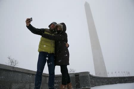 A couple pauses to take a 'selfie' in the freshly fallen snow near the Washington Monument in Washington January 22, 2016. REUTERS/Jonathan Ernst