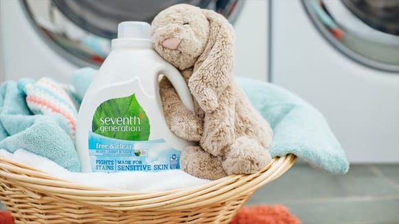 A laundry basket fille with towels, laundry detergent, and a stuffed rabbit.