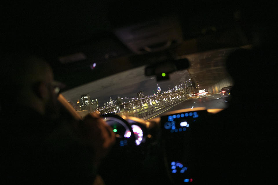 Mohamed Bahe, 36 director of the Muslim Community Center, left, drives with other volunteers towards an illuminated Brooklyn Bridge and New York City skyline on the way to Herald Square in Manhattan on Monday, April 27, 2020. They hand out food to the hungry, as part of their Need2Feed project which will have them giving out food every night for the month of Ramadan, in New York. (AP Photo/Wong Maye-E)