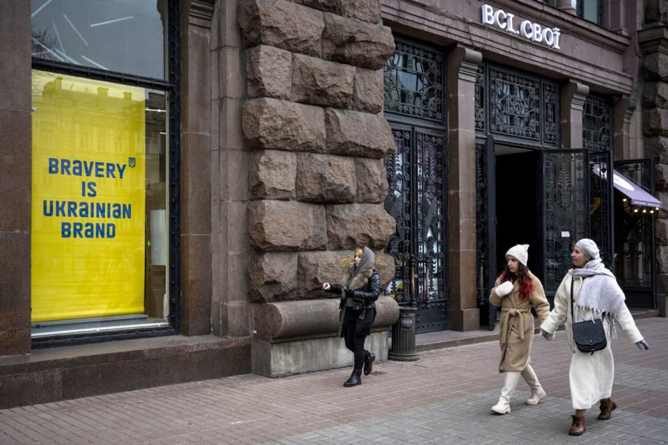 Women walk past a billboard reading, "Bravery is Ukrainian Brand."