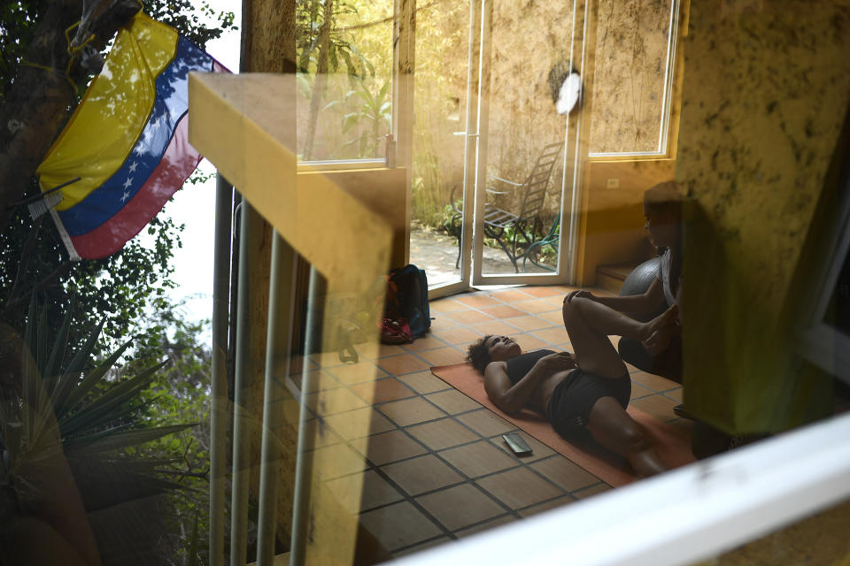 Fotografiada a través de una ventana, la venezolana Stefany Hernández, medallista olímpica en BMX, realiza una fisioterapia dentro de su casa en Caracas, el lunes 25 de mayo de 2020 (AP Foto/Matías Delacroix)