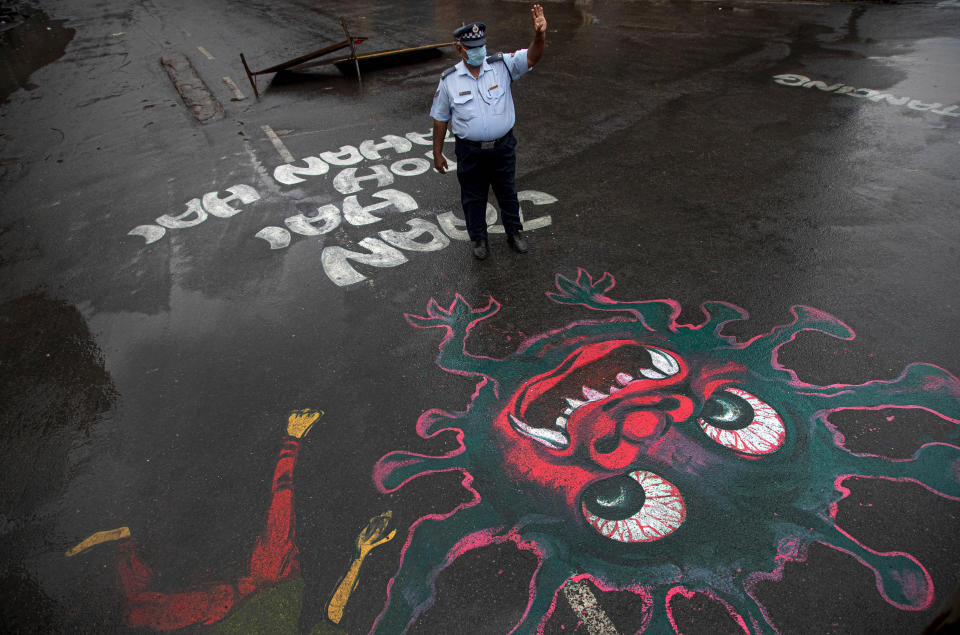 An Indian traffic policeman stands next to an artwork displayed on a road to create awareness about coronavirus during lockdown in Gauhati, India, Wednesday, April 15, 2020. Indian Prime Minister Narendra Modi on Tuesday extended the world's largest coronavirus lockdown to head off the epidemic's peak, with officials racing to make up for lost time. (AP Photo/Anupam Nath)