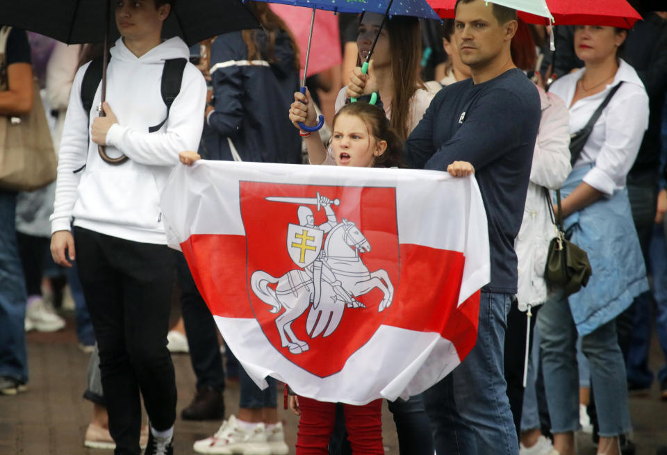 A girl holds an old Belarusian national flag as people gather next to Ministry of Internal Affairs of Belarus in Minsk, Belarus, Wednesday, Aug. 19, 2020. The authoritarian leader of Belarus complained that encouragement from abroad has fueled daily protests demanding his resignation as European Union leaders held an emergency summit Wednesday on the country's contested presidential election and fierce crackdown on demonstrators. (AP Photo/Dmitri Lovetsky)