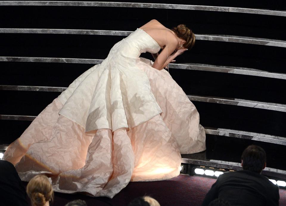 Jennifer in a white ballgown with an oversized skirt. She is hunched over with her hand on her head falling up stage stairs.