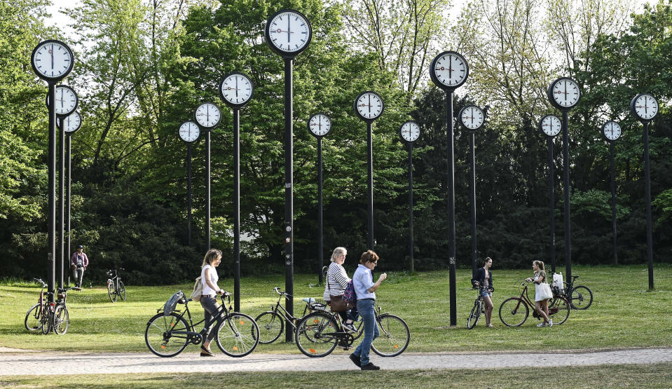 FILE - People with bicycles meet at the clock park in Duesseldorf, Germany, Friday, April 24, 2020. Once again, most Americans will set their clocks forward by one hour this weekend, losing perhaps a bit of sleep but gaining more glorious sunlight in the evenings as the days warm into summer. How we came to move the clock forward in the spring, and then push them back in the fall, is a tale of that spans over a century and is one that's been driven by two world wars, mass confusion at times and a human desire to bask in the sun for a long as possible after finishing work. There's been plenty of debate over the practice but about 70 countries — about 40 percent of those across the globe — currently use what Americans call daylight saving time. (AP Photo/Martin Meissner, File(