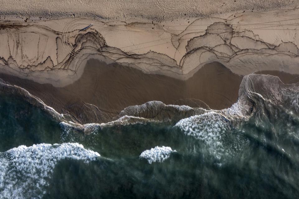 A drone view of a beach with oil scattered on the sand.