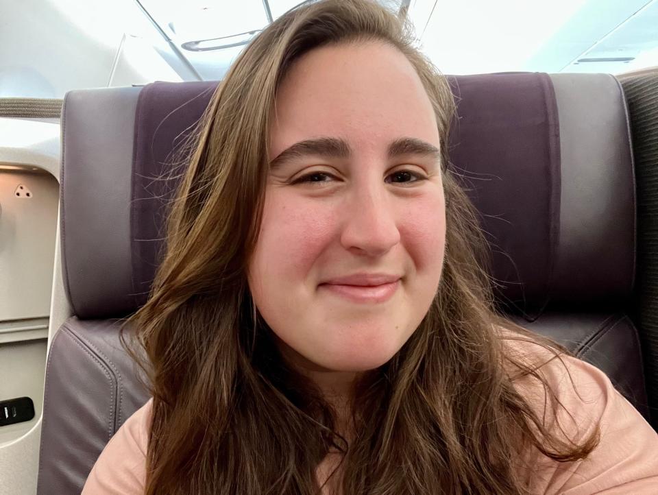 A selfie of the author in the business class seat wearing a pink shirt.