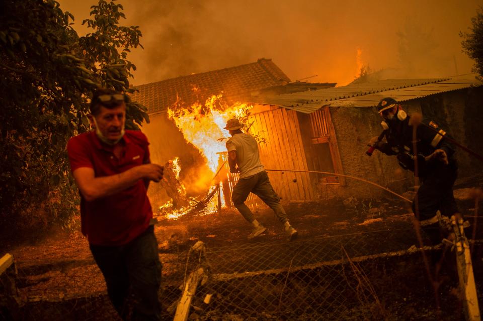 TOPSHOT - A firefighter and locals rush to a burning house in an attempt to extinguish forest fires that are approaching the village of Pefki on Evia (Euboea) island, Greece's second largest island, on August 8, 2021. - Hundreds of Greek firefighters fought desperately on August 8 to control wildfires on the island of Evia that have charred vast areas of pine forest, destroyed homes and forced tourists and locals to flee. Greece and Turkey have been battling devastating fires for nearly two weeks as the region suffered its worst heatwave in decades, which experts have linked to climate change. (Photo by ANGELOS TZORTZINIS / AFP) (Photo by ANGELOS TZORTZINIS/AFP via Getty Images)
