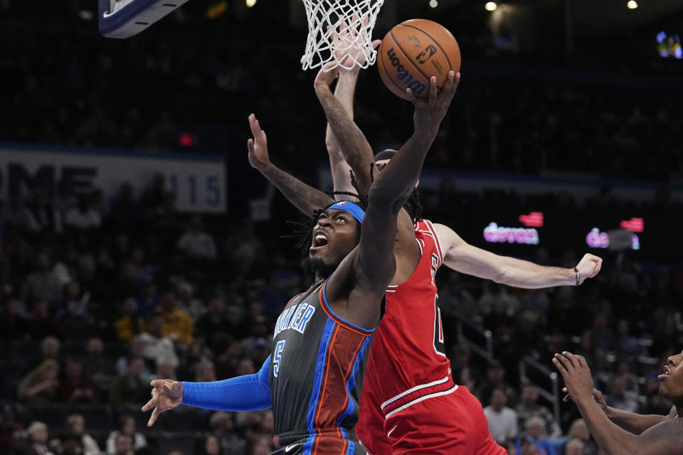 Oklahoma City Thunder forward Luguentz Dort (5) goes to the basket in front of Chicago Bulls guard Coby White, center, and Alex Caruso, rear, in the first half of an NBA basketball game Friday, Nov. 25, 2022, in Oklahoma City. (AP Photo/Sue Ogrocki)