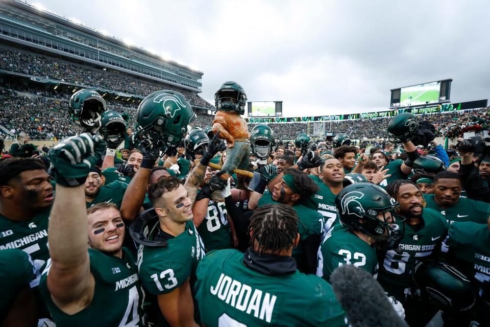 Michigan State players hold up the Paul Bunyan trophy in celebration after its win over Michigan.