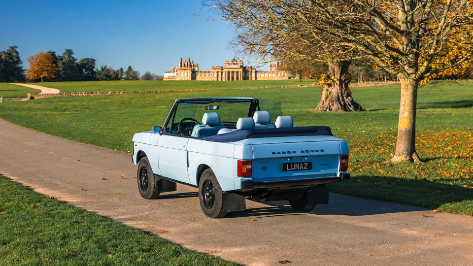 a blue two door convertible range rover sits on a road in a park
