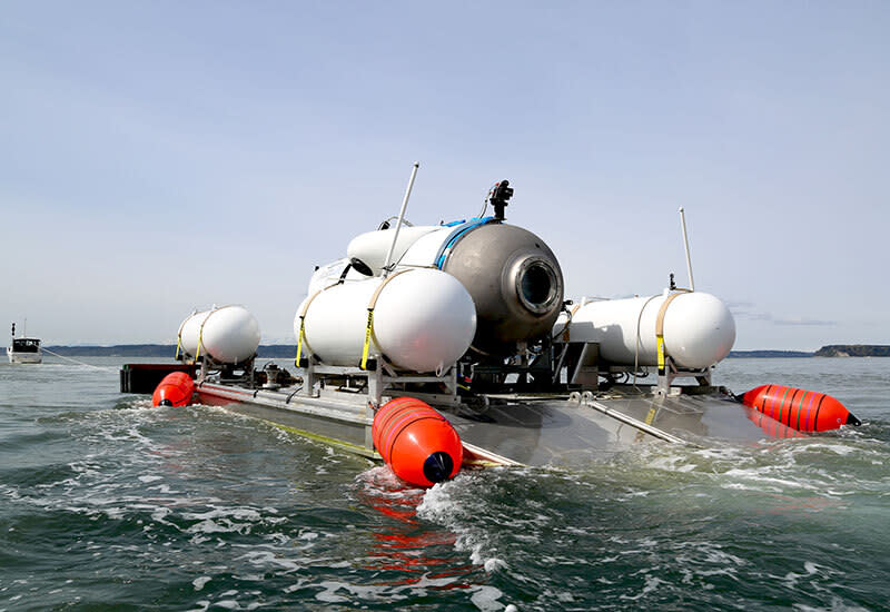 OceanGate's tourist submersible on the surface of the sea, supported by four red floats, and with two white canisters on either side. The coast is visible in the distance. 