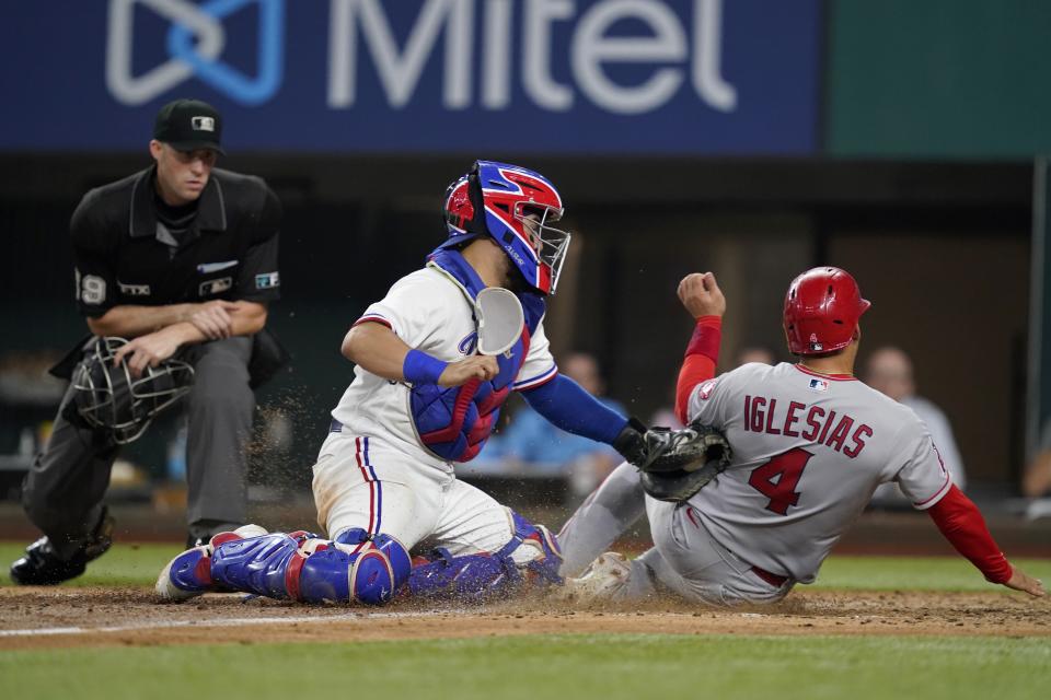 Home plate umpire Nic Lentz, left, looks on as Texas Rangers catcher Jose Trevino, center, tags out Los Angeles Angels' Jose Iglesias (4) who was trying to score on a Brandon Marsh double in the sixth inning of a baseball game in Arlington, Texas, Tuesday, Aug. 3, 2021. (AP Photo/Tony Gutierrez)