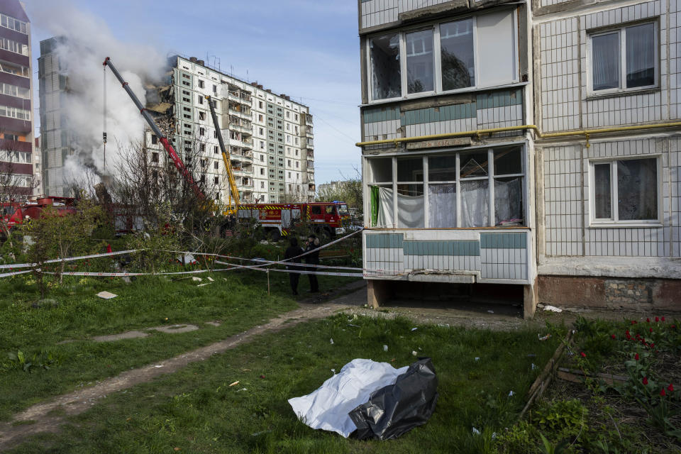 Bodies recovered from a residential area that was hit during a Russian attack lie on the ground as firefighters, in the background, try to extinguish a fire in Uman, central Ukraine, Friday, April 28, 2023. (AP Photo/Bernat Armangue)