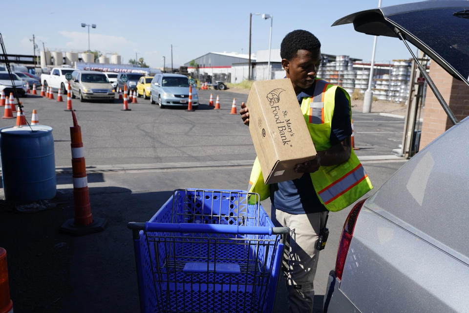 A volunteer fills up a vehicle with food boxes at the St. Mary's Food Bank as dozens of vehicles line up in the background Wednesday, June 29, 2022, in Phoenix. Long lines are back at food banks around the U.S. as working Americans overwhelmed by inflation turn to handouts to help feed their families. (AP Photo/Ross D. Franklin)