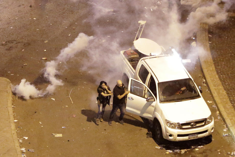 In this Friday Oct. 18, 2019 photo, Lebanese reporter Joyce Akiki, left, runs from tear gas during an anti-government protest, in Beirut, Lebanon. Lebanese journalists are facing wide-ranging harassment and obstacles to their work - including verbal insults and physical attacks, even death threats - amid reporting on nearly 50 days of anti-government protests, drawing into question Lebanon’s reputation as a haven for free speech in a troubled region. (AP Photo/Hassan Ammar)