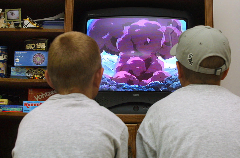 Two people watching a mushroom cloud explosion on an old television set