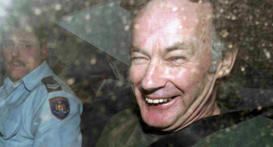 A file photo of NSW serial killer Ivan Milat in a police car in 1997. Smiling out the window at the camera.