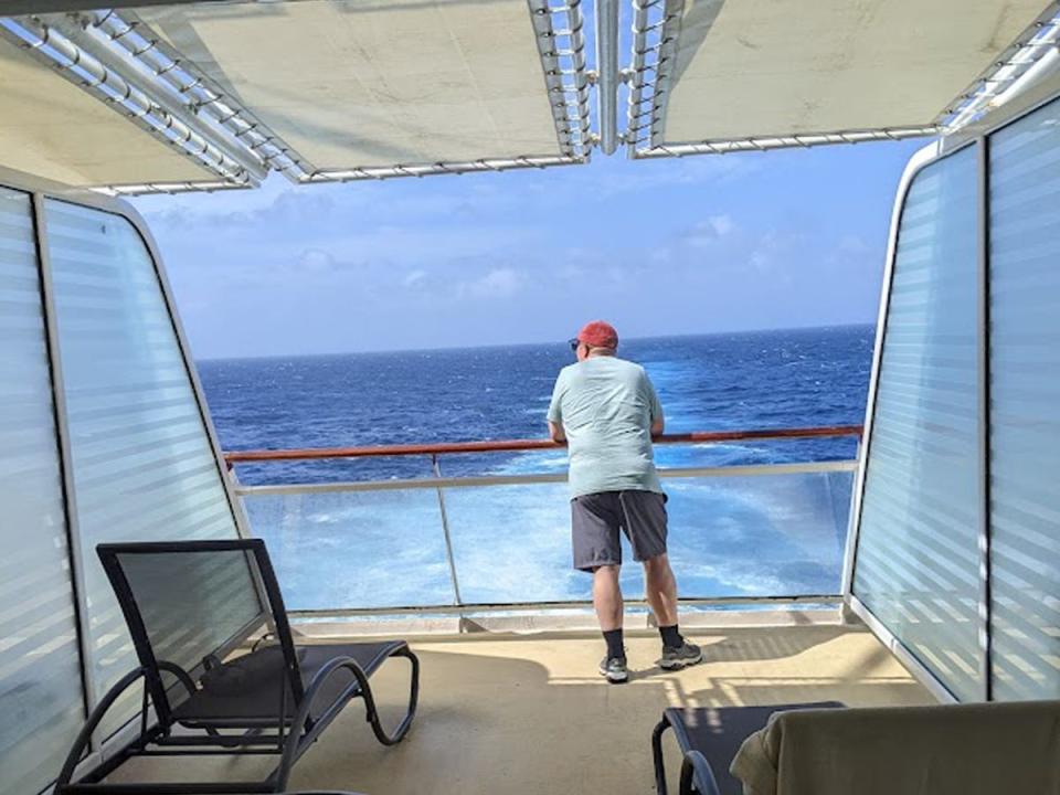Renae Gregoire's husband leaning on the balcony of their cabin and looking out to sea on a Celebrity Cruises ship.