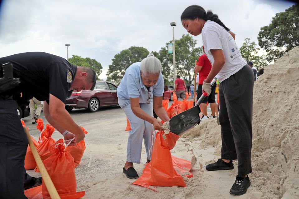 Joan Chang, center, gets help filling her bags during a sandbag giveaway in preparation for Hurricane Dorian, Friday, Aug. 30, 2019, in Margate, Fla.