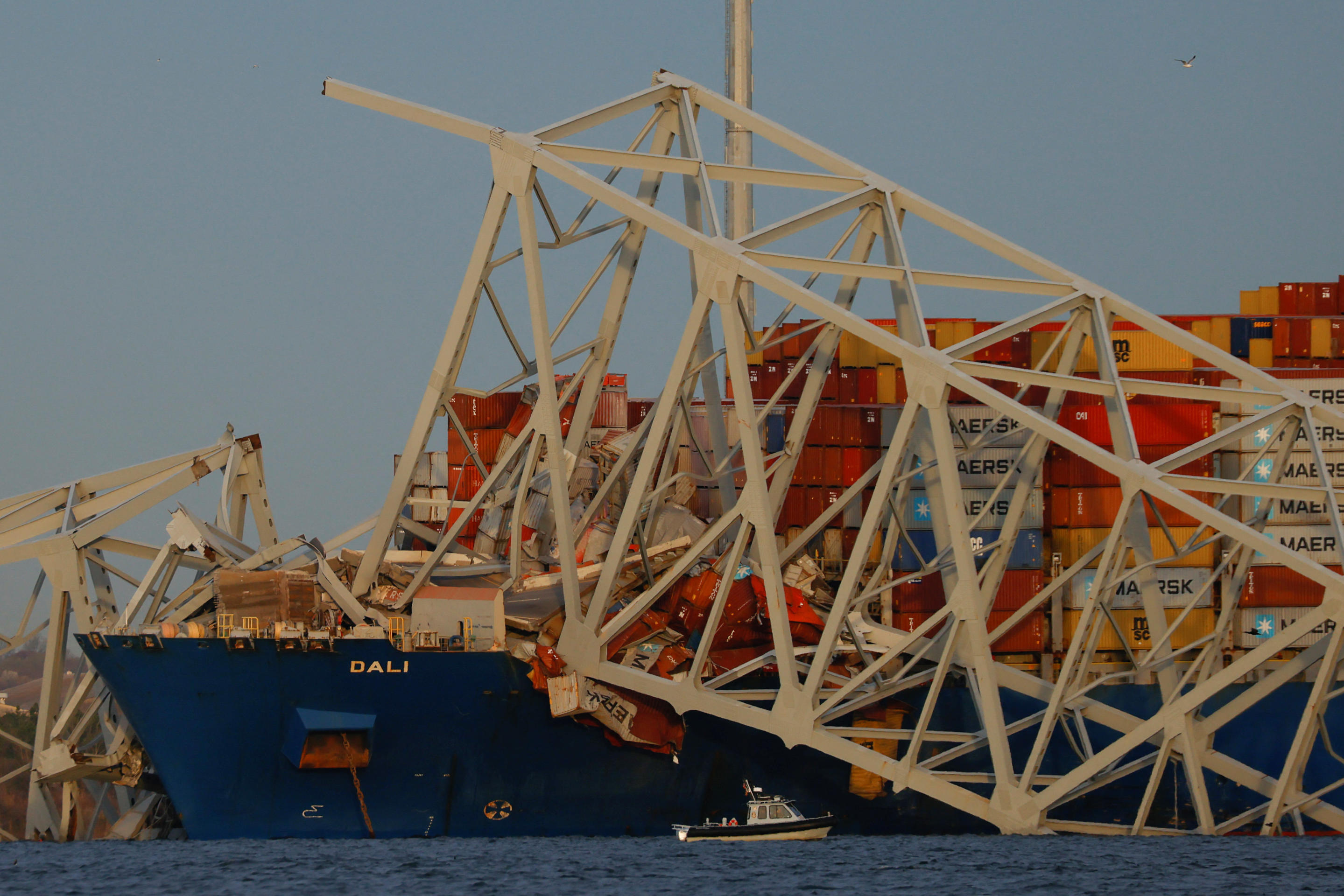 Container ship amid twisted metal sections of destroyed bridge.