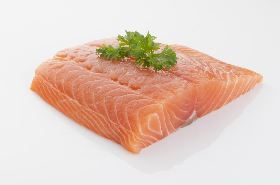 Raw piece of salmon with cilantro garnish on a white background.