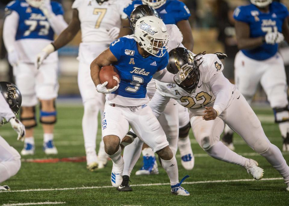 FILE - Tulsa's Shamari Brooks, left, tries to fight off Central Florida defensive lineman Kalia Davis during an NCAA college football game in Tulsa, Okla., in this Friday, Nov. 8, 2019, file photo. Most of the top college football players who opted out of the 2020 season due to the pandemic decided to leave school and launch their pro careers. But plenty of other players who opted out of last season chose to continue their college careers either at their original school or opted to transfer. Kalia Davis Davis started each of UCF's final nine games in 2019 and ended that season with 27 tackles, including eight for loss. (Brett Rojo/Tulsa World via AP, File)