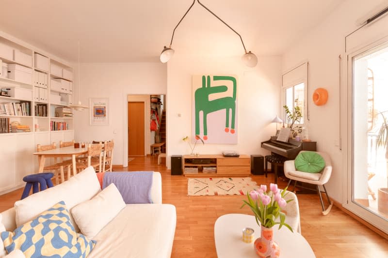 White living room with white sofa, piano, bold art, and dining area in background