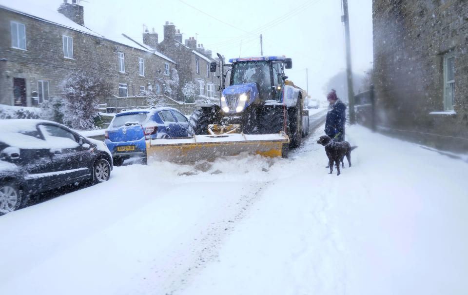 A snow plough passes a woman and her dog in Bowes, Durham.